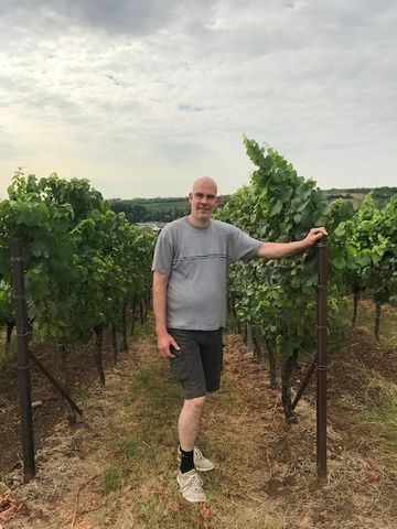 Ein Mann steht in einem Weinberg neben einem Zaun.