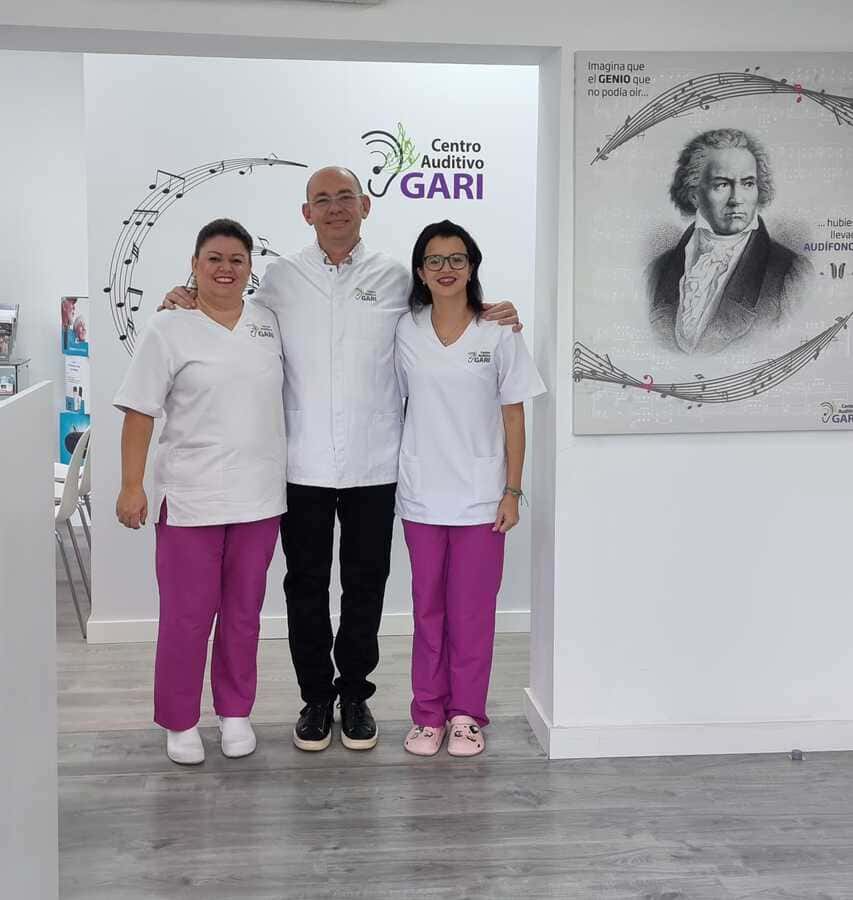 Un hombre y dos mujeres posan para una foto frente a un cartel que dice centro de gari