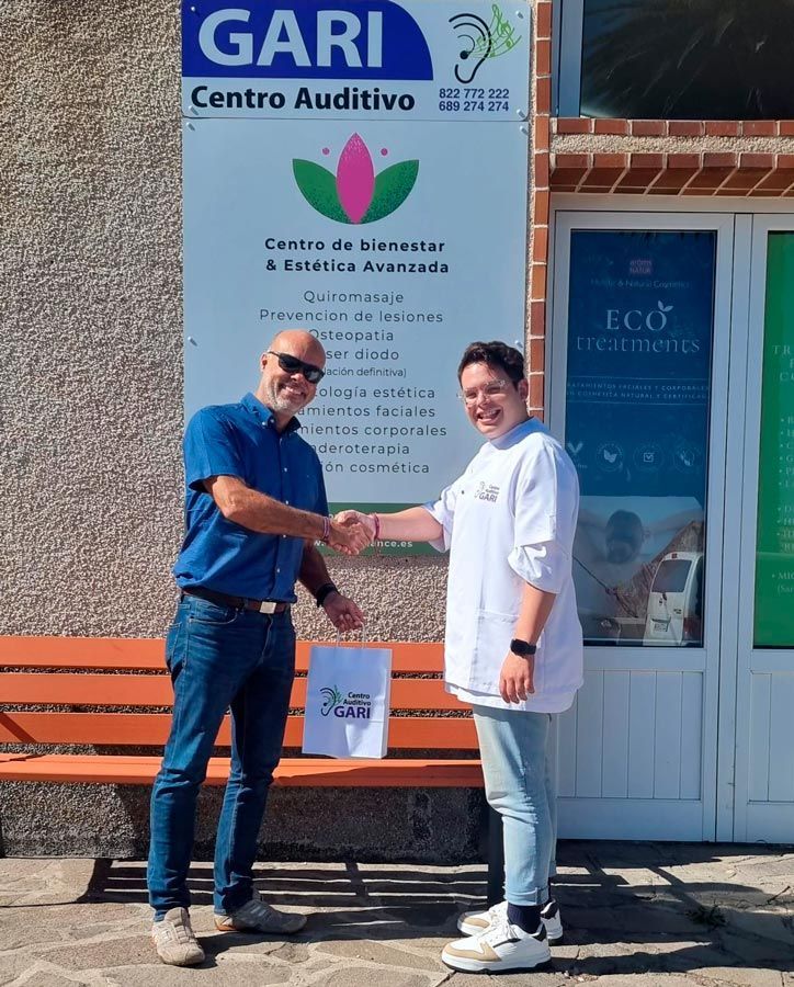 Un hombre y una mujer se dan la mano frente a un cartel que dice gari centro auditivo
