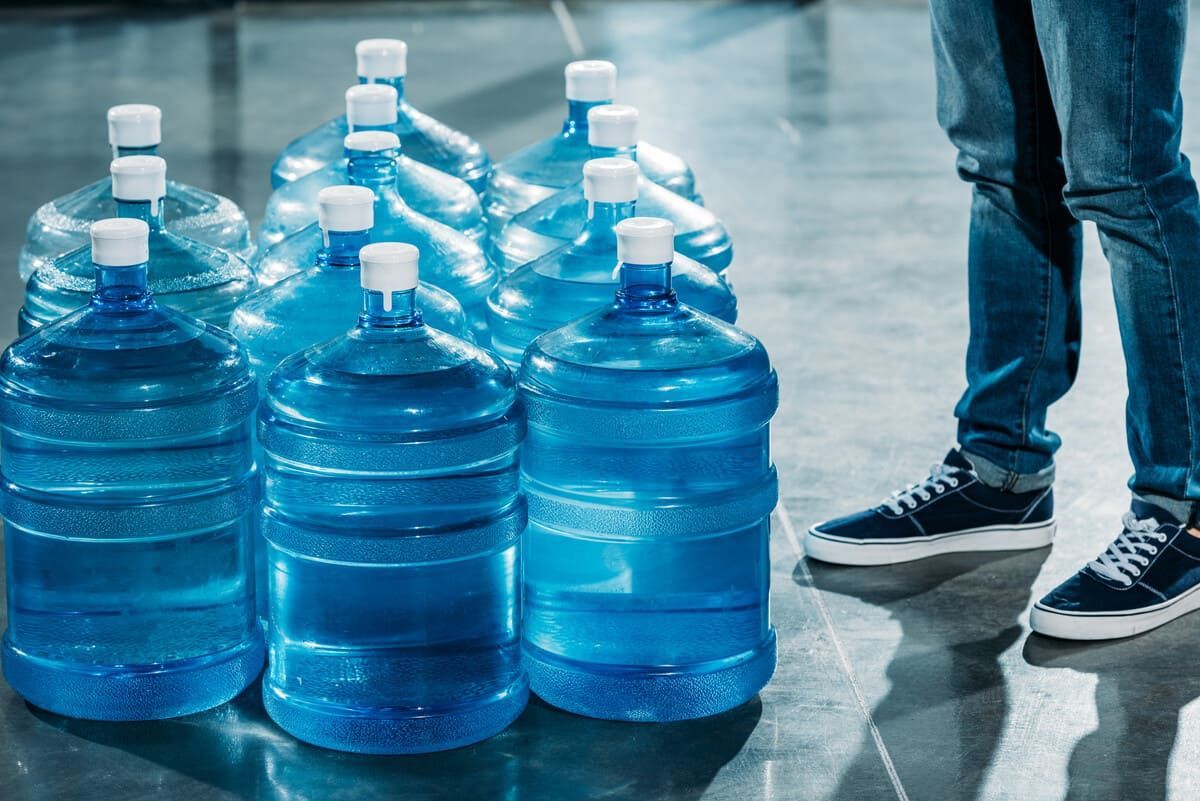 Un hombre está de pie junto a una pila de botellas de agua.