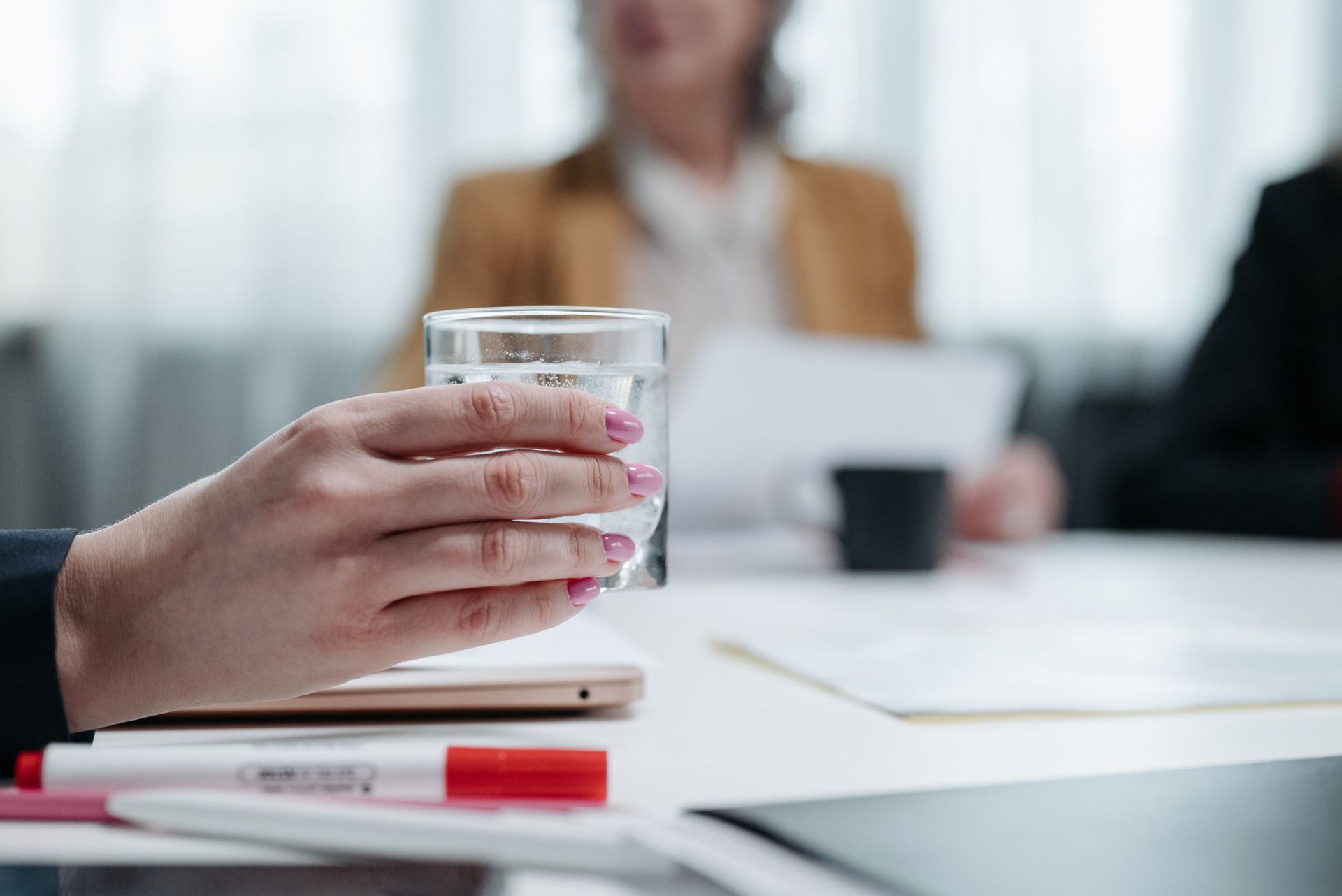 Una mujer está sentada en una mesa sosteniendo un vaso de agua.
