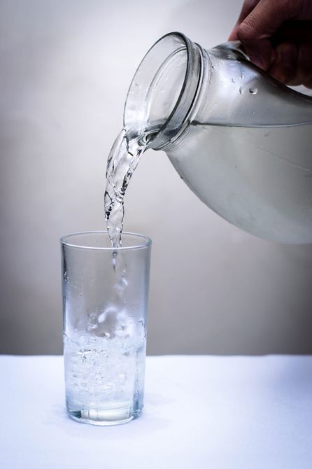 Una persona está vertiendo agua en un vaso sobre una mesa.