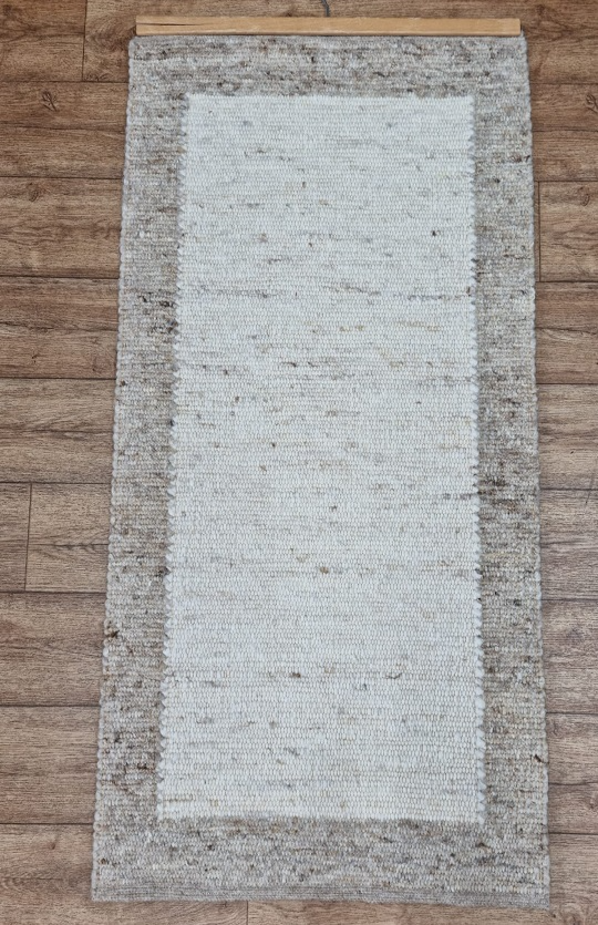 Auf einem Holzboden liegt ein weißer Teppich mit braunem Rand.