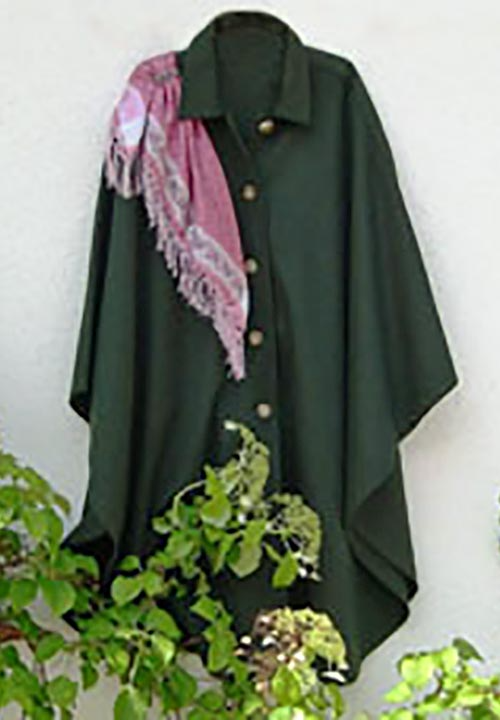 Ein grüner Umhang mit einem rosa Schal hängt an einer Wand.