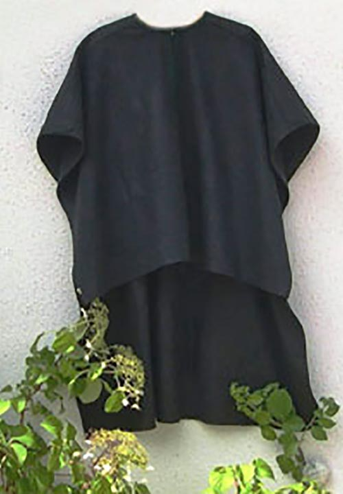 Ein schwarzer Poncho hängt an einer weißen Wand neben einer Pflanze.