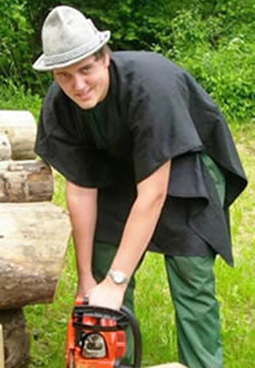 Ein Mann mit Hut schneidet mit einer Kettensäge einen Baumstamm