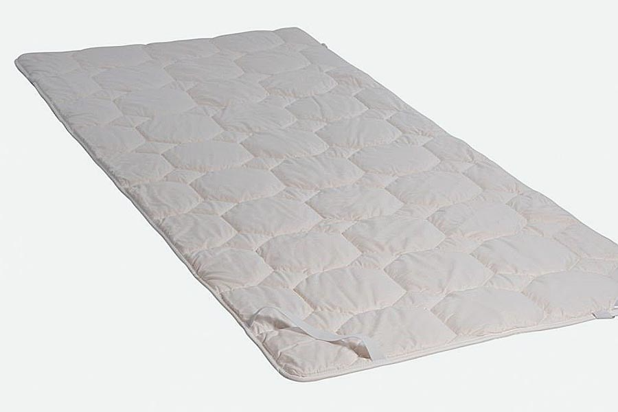 Eine weiße Matratzenauflage liegt auf einer weißen Oberfläche.