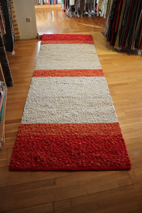 Auf einem Holzboden liegt ein rot-weiß gestreifter Teppich.