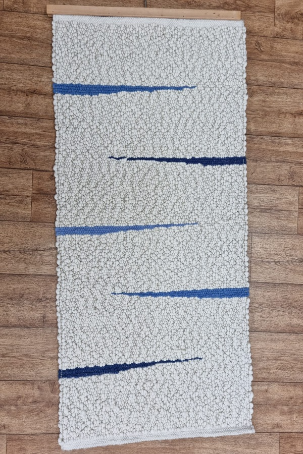Auf einem Holzboden liegt ein weißer Teppich mit blauen Streifen.