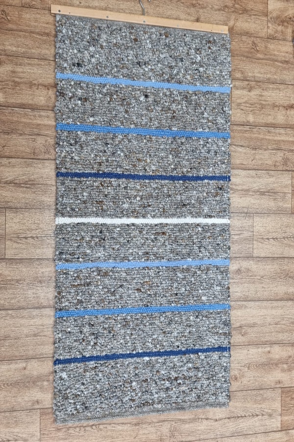 Ein grauer Teppich mit blauen Streifen hängt an einer Holzwand