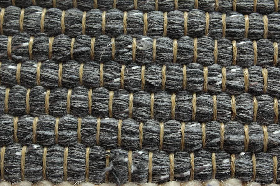 Eine Nahaufnahme eines grauen Teppichs mit braunen Nähten