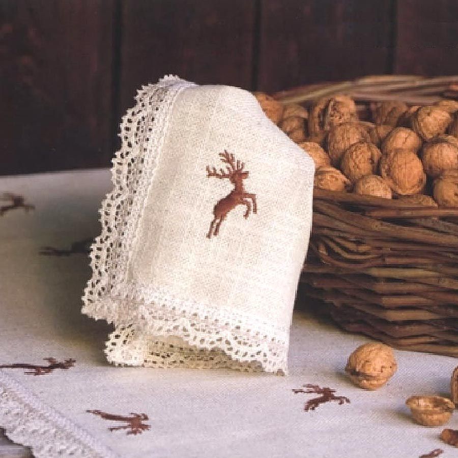 Eine Serviette mit einem aufgestickten Hirsch liegt neben einem Korb mit Walnüssen