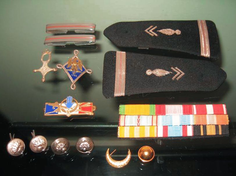 Une collection d'insignes militaires, comprenant des épaulettes, des médailles, des rubans et des boutons d'uniforme, sur une surface sombre.