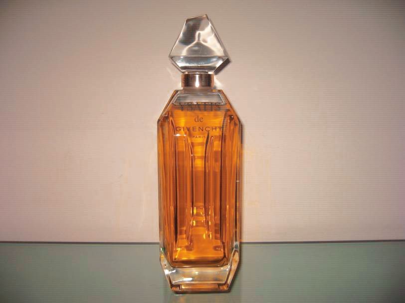 Une bouteille en verre transparent à facettes, remplie d'un liquide ambré, surmontée d'un bouchon géométrique à l'aspect cristallin.