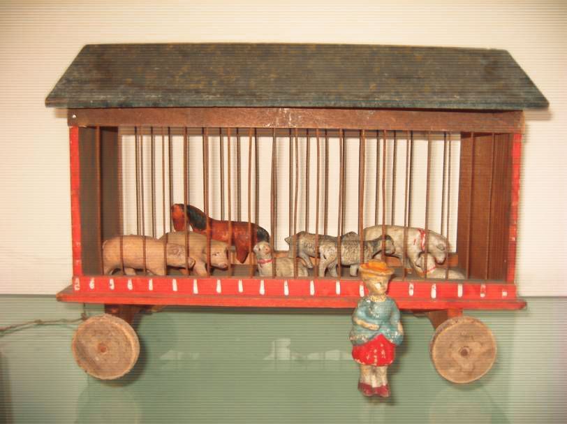 Un wagon de cirque miniature vintage avec des barres, contenant des figurines d'animaux miniatures et une petite figurine debout à l'avant.