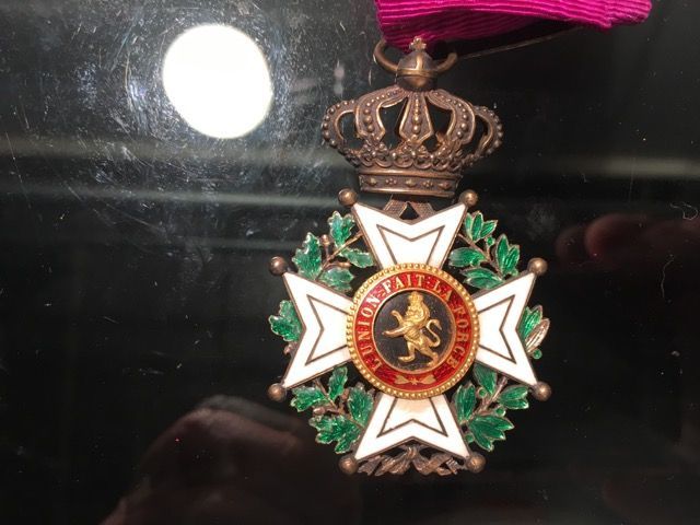 Une médaille de l'Ordre de Léopold avec une croix blanche, une couronne verte et un emblème central de lion portant l'inscription « L'UNION FAIT LA FORCE ».