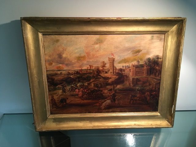 Une peinture à l'huile sous cadre doré représentant un paysage champêtre avec une tour en pierre, des personnages et un ciel chargé d'atmosphère.