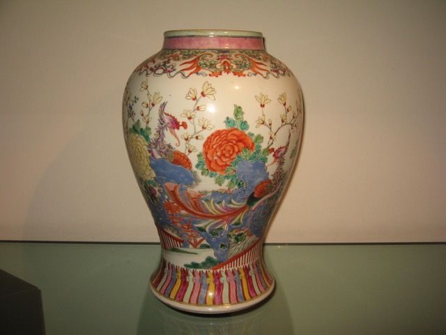 Un vase décoratif en porcelaine de style chinois orné de motifs floraux colorés, de créatures mythiques bleues et de bordures rayées.