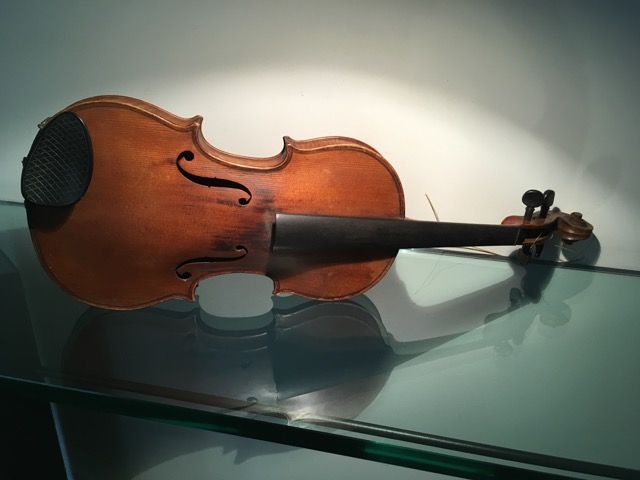 Un violon brun avec un mentonnière noire repose sur une surface en verre réfléchissante, sur un fond faiblement éclairé.