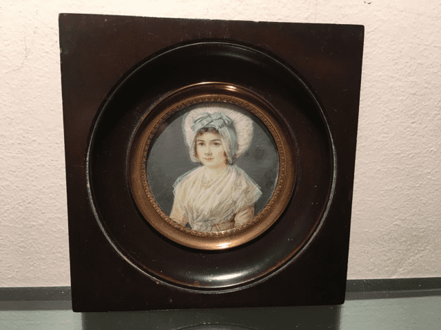 Un portrait miniature circulaire d'une personne portant une coiffe bleu pâle et un châle blanc, encadré dans un cadre en bois foncé.