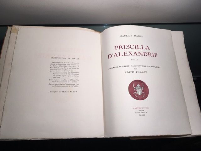 Un livre ouvert montrant la page de titre de Priscilla d'Alexandrie avec un petit emblème circulaire rouge en bas.