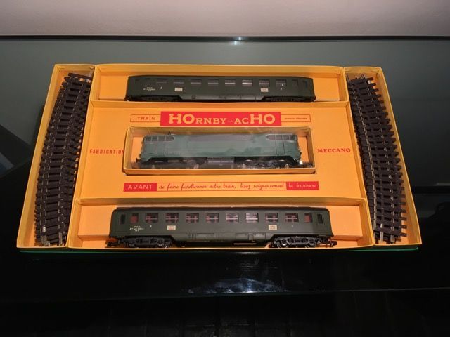 Un coffret de train miniature Hornby-Acho vintage à l'échelle HO dans une boîte jaune, comprenant une locomotive, deux wagons et des rails courbes.