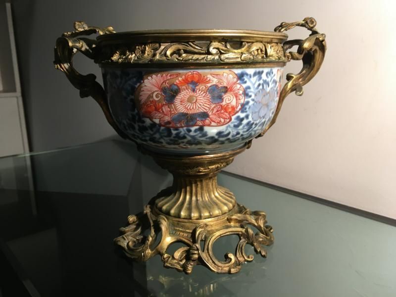 Un bol en porcelaine orné de motifs floraux rouges et bleus, monté sur un socle en métal doré finement travaillé, muni de poignées latérales.