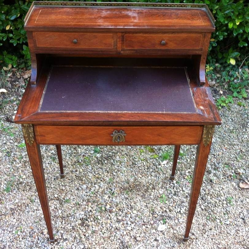 Un bureau ancien en bois avec deux petits tiroirs supérieurs, un plateau en cuir foncé, un tiroir principal et des ornements en laiton.