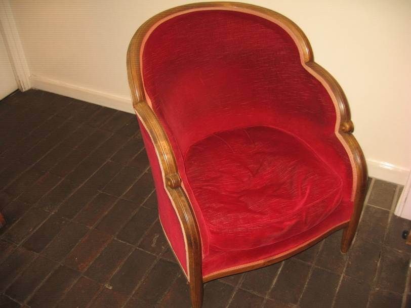 Un fauteuil en velours rouge de style tonneau avec une structure en bois courbée, sur un sol carrelé foncé.
