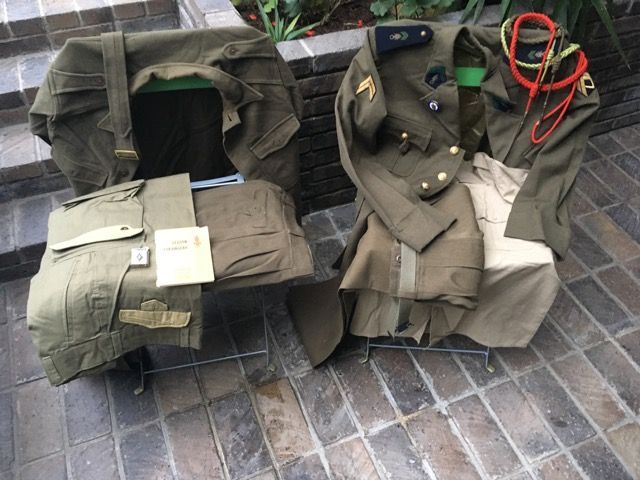 Deux uniformes militaires d'époque, avec leurs accessoires, sont disposés sur des chaises sur une terrasse en pierre.