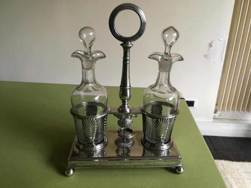 Un ensemble à condiments en métal argenté composé de deux flacons en verre avec bouchons, reposant sur une base rectangulaire munie d'une poignée centrale.