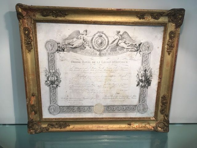 Un cadre ancien orné de dorures, contenant un certificat de la Légion d'honneur française avec des gravures décoratives et un sceau de cire.