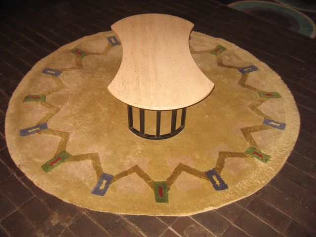 Une table basse claire aux bords arrondis est placée au centre d'un grand tapis rond beige orné d'un motif géométrique en zigzag.