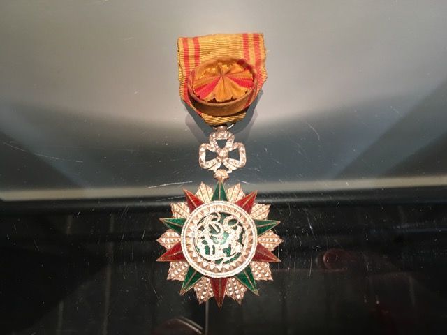 Médaille marocaine de l'Ordre d'Ouissam Alaouite avec un pendentif en forme d'étoile, des rayons rouges et verts bordés d'or et un ruban jaune.
