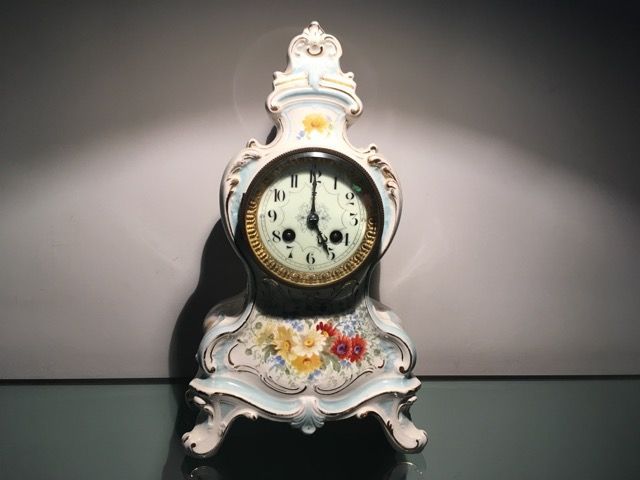 Une pendule de cheminée en porcelaine bleu clair ornée de motifs floraux peints sur fond sombre.