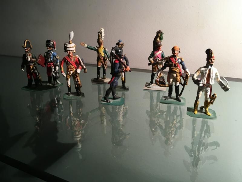 Une rangée de soldats de plomb historiques peints à la main, vêtus d'uniformes militaires colorés, se tenant sur une surface en verre réfléchissante.
