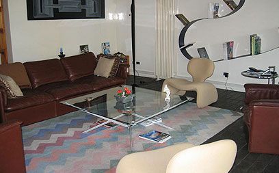 Un salon moderne avec un canapé en cuir marron, une table basse en verre, un tapis à motifs et des fauteuils sculpturaux beiges.