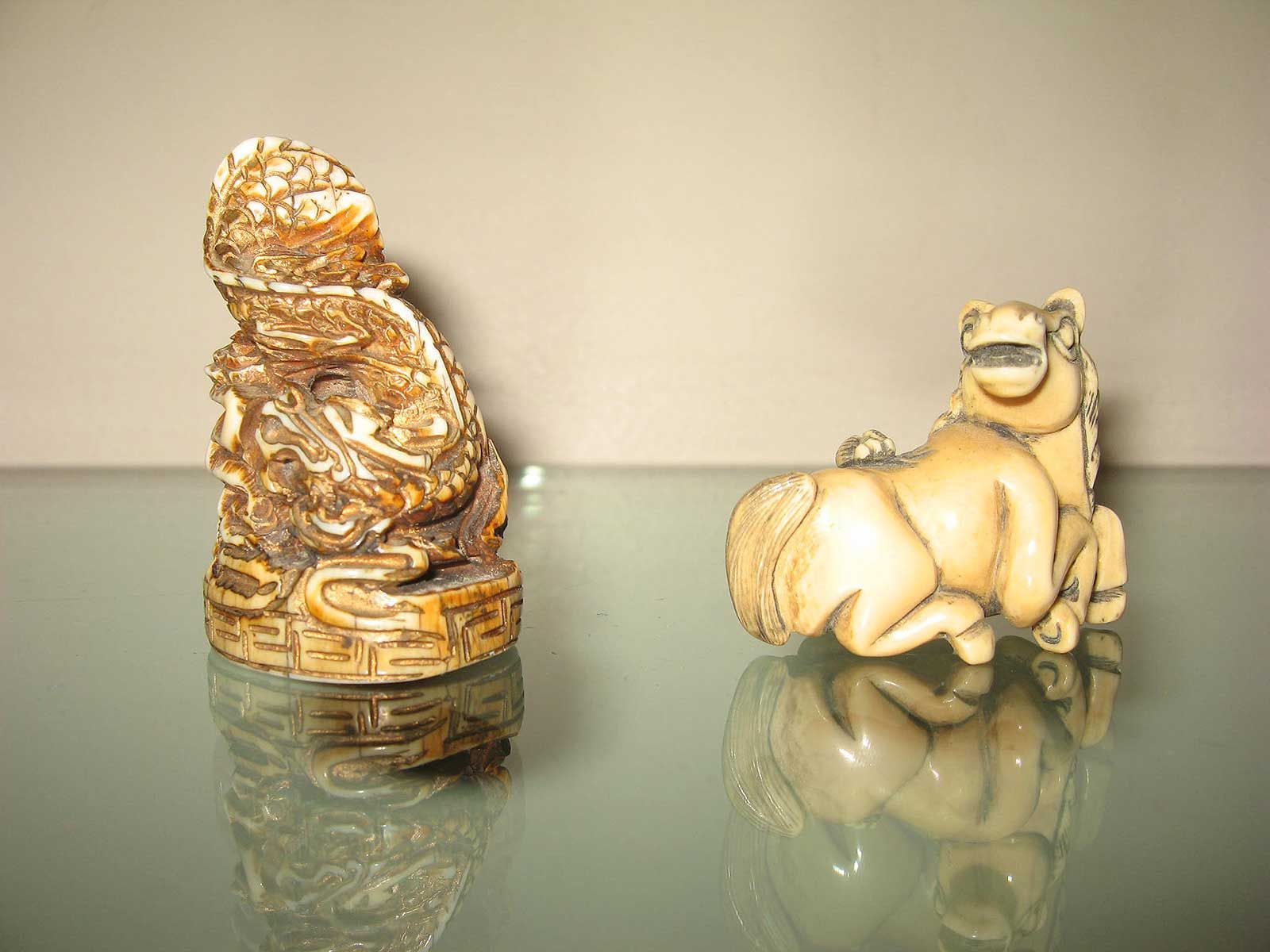 Deux figurines sculptées dans le style de l'ivoire, un dragon texturé et un cheval lisse, sont posées sur une surface en verre réfléchissant.