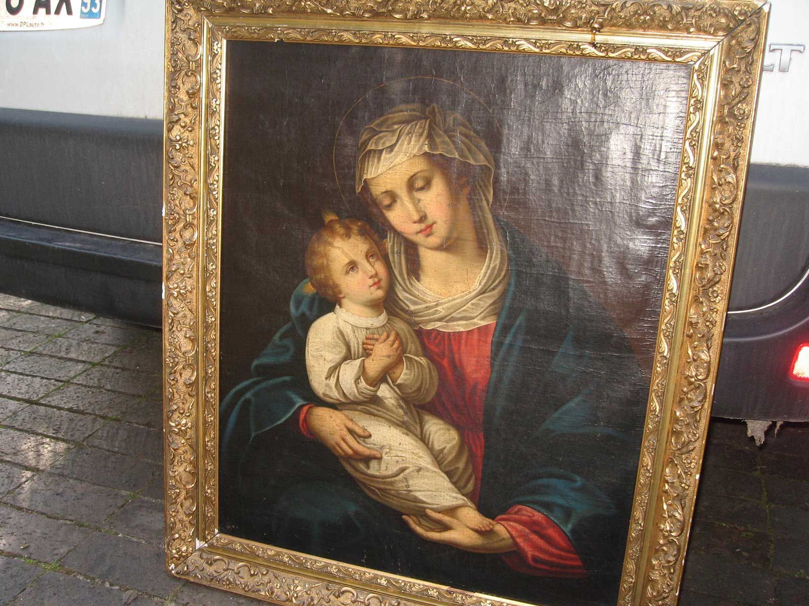Un tableau classique sous cadre doré représentant une femme vêtue de rouge et d'un manteau bleu tenant un jeune enfant.