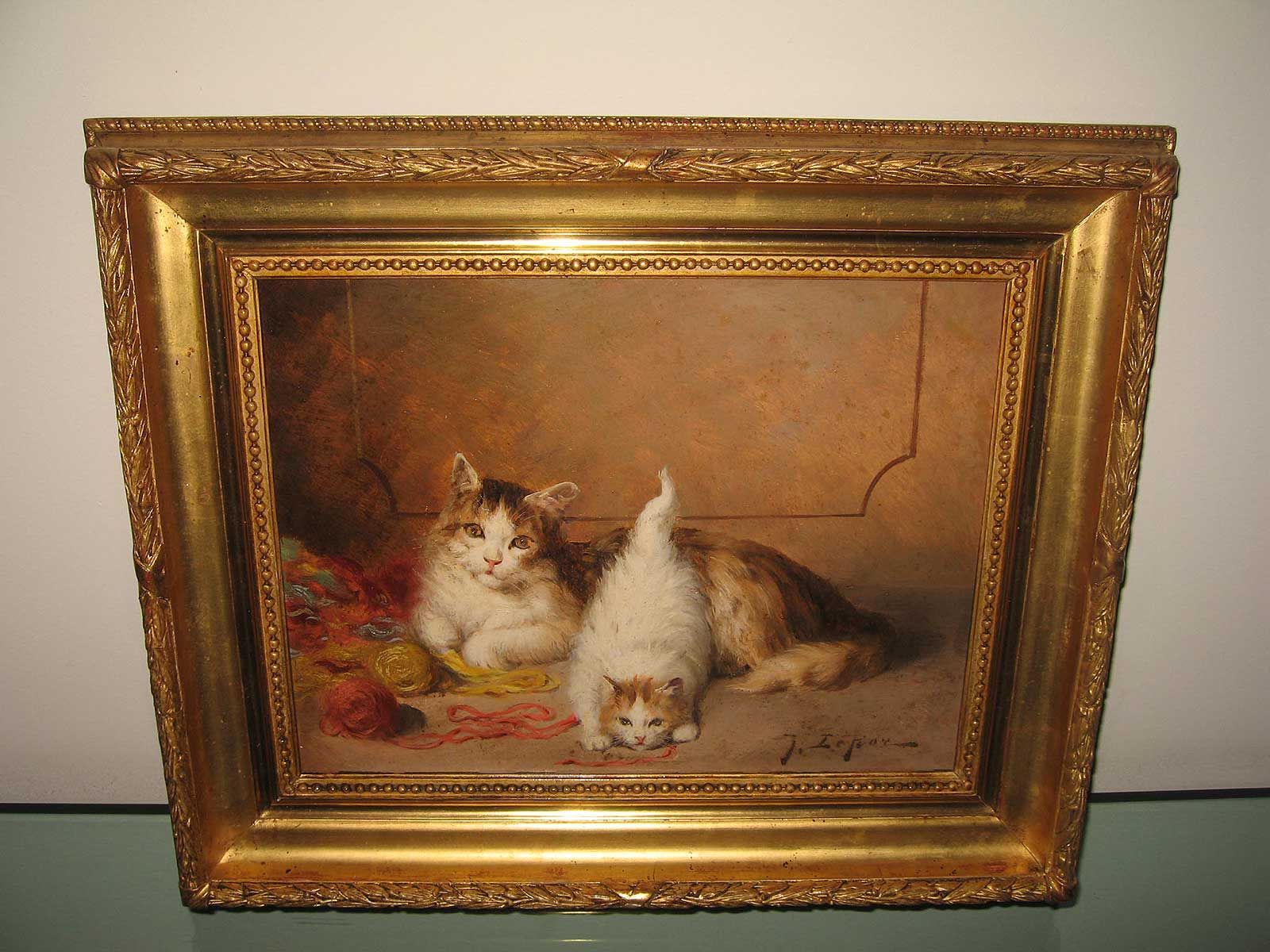 Un tableau à l'huile représente deux chats jouant avec des pelotes de laine dans une pièce chaleureuse et faiblement éclairée, le tout encadré d'un cadre doré orné.