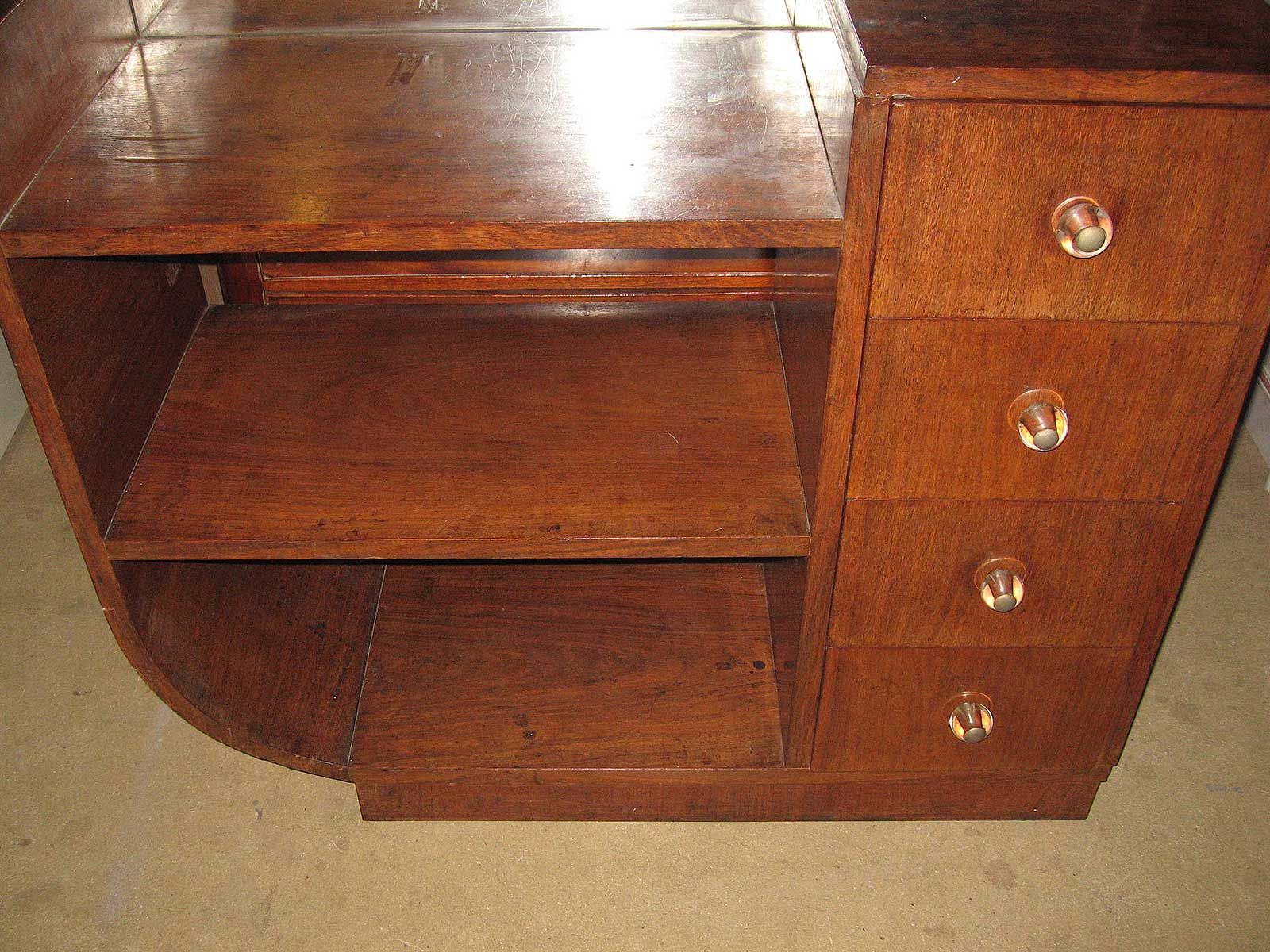 Une coiffeuse ou une table d'appoint en bois brun avec une étagère ouverte incurvée et quatre tiroirs à poignées en verre.