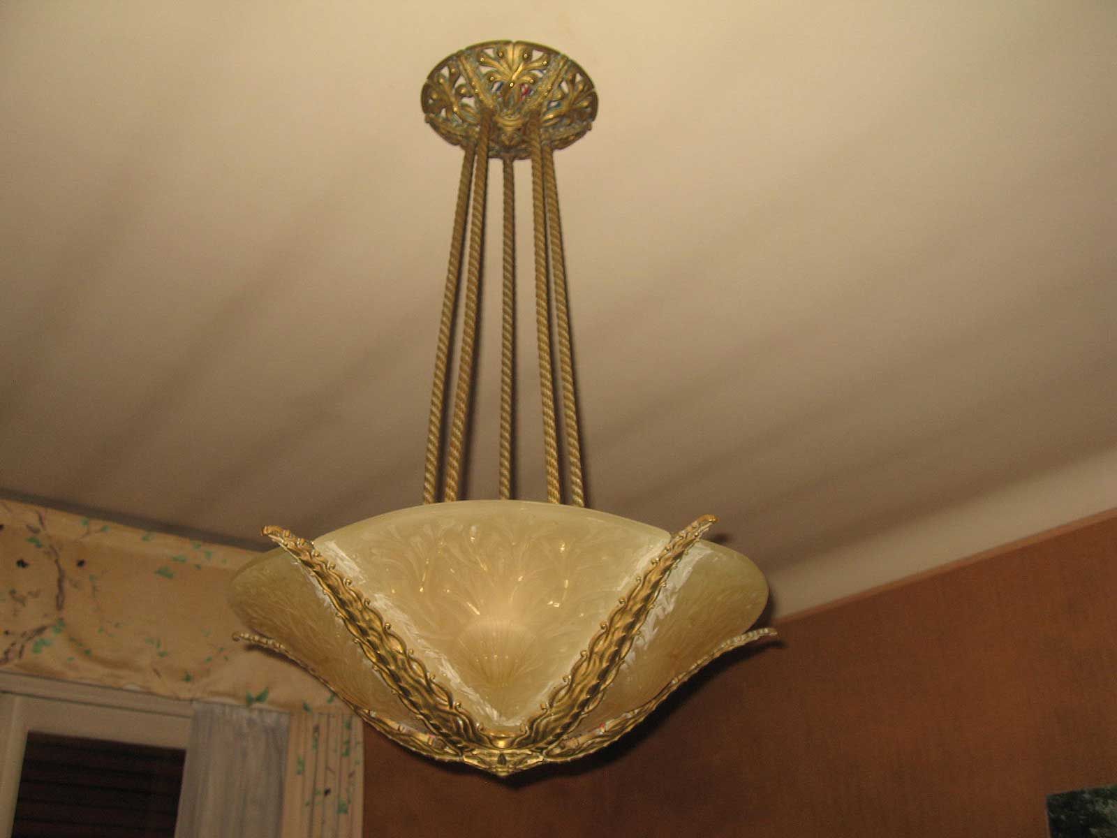 Un luminaire suspendu en laiton orné, de style vintage, avec un large abat-jour en verre dépoli suspendu par des chaînes métalliques.