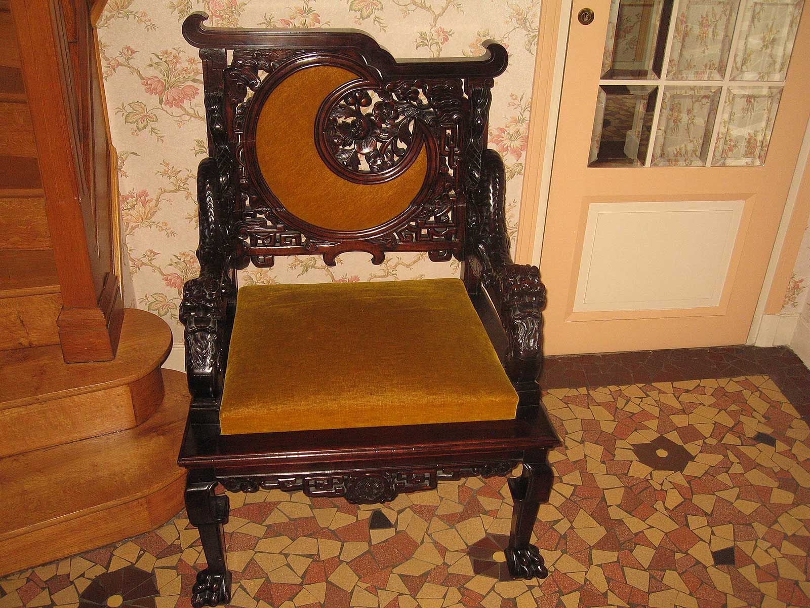 Une chaise en bois sombre ornée, avec un croissant de lune découpé dans le dossier et une assise en velours jaune moutarde.