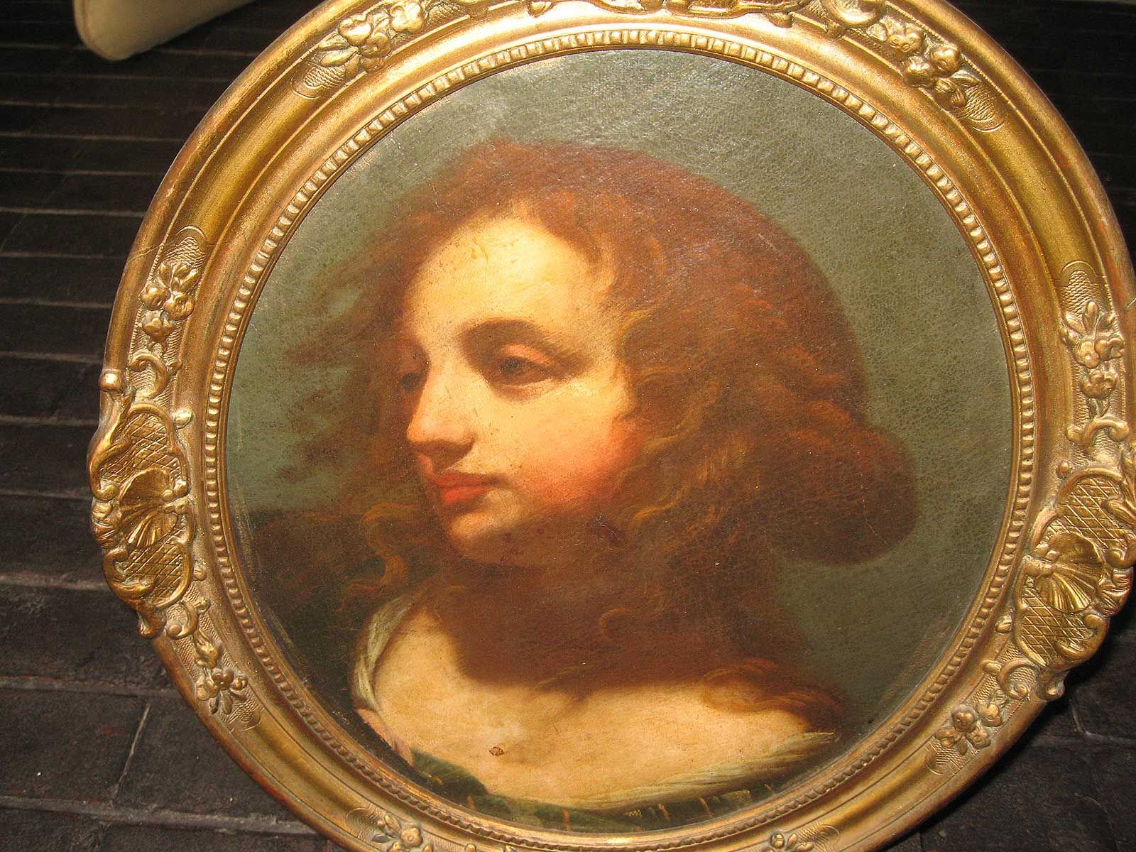 Une peinture à l'huile représentant une personne aux cheveux longs et flottants, dans un cadre ovale doré orné et décoratif, sur fond sombre.