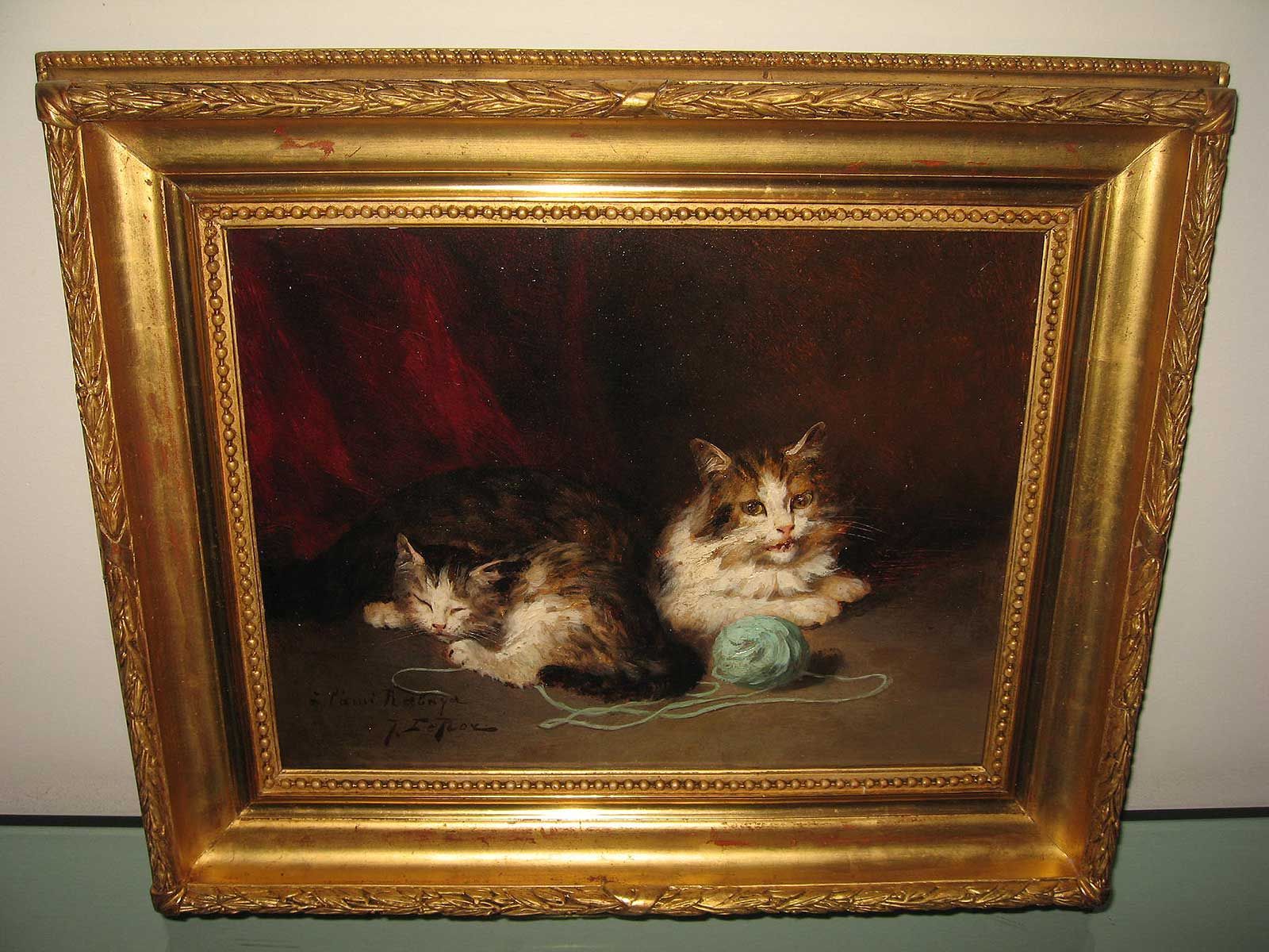 Tableau à l'huile encadré représentant deux chats duveteux se reposant près d'une pelote de laine sur un fond sombre orné de rideaux rouges.