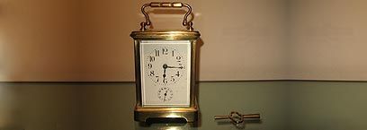 Une pendule de voyage dorée, à cadran blanc et à clé de remontage séparée, repose sur une surface réfléchissante.