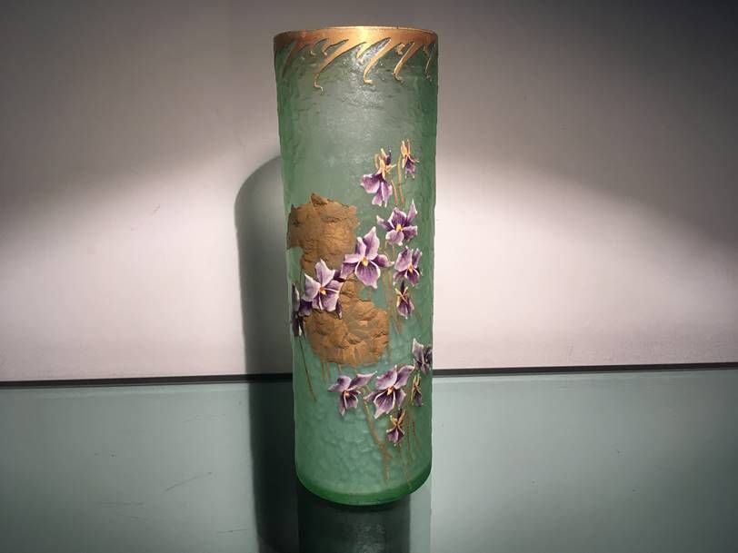 Un grand vase cylindrique en verre vert dépoli, orné de fleurs violettes peintes à la main, de détails en feuille d'or et d'un liseré doré.