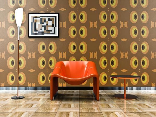 Une chaise orange est placée sur un parquet devant un papier peint marron à motifs, à côté d'une grande lampe et d'une petite table.