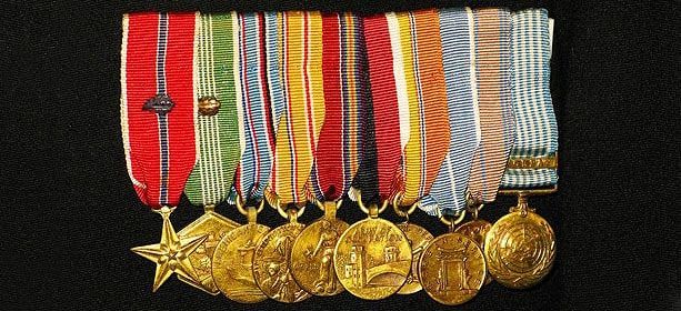 Une rangée de dix médailles de campagne militaire, ornées de rubans colorés, se détache sur un fond sombre.