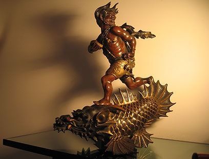Sculpture en bronze représentant un personnage courant sur un dragon stylisé doré en forme de poisson, sur fond uni.
